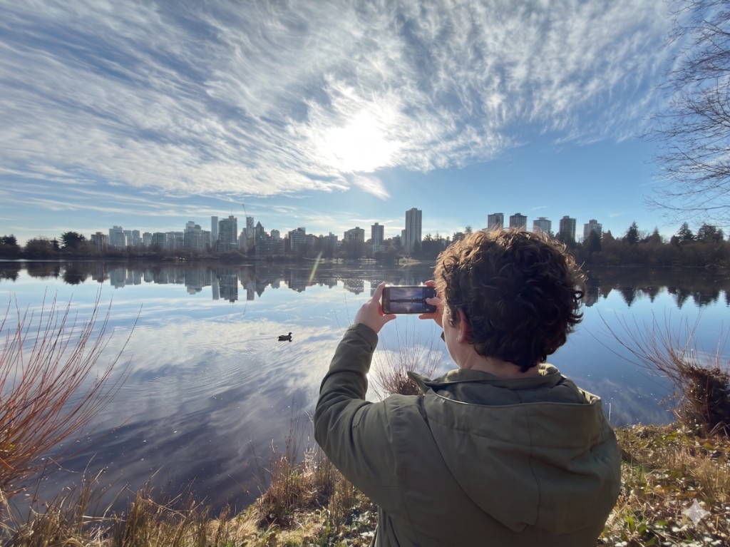 Person photographing a city skyline across calm water with a smartphone